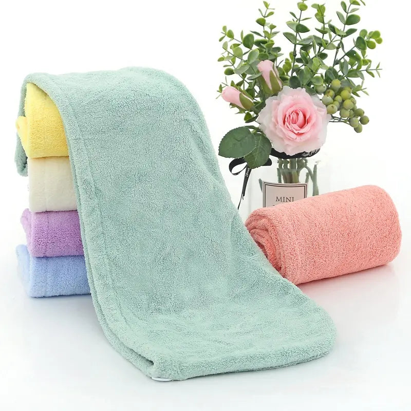 Serviette de séchage des cheveux. Une serviette verte étalée et 5 pliées en rouleaux a coté. Jaune, beige, mauve, bleue et saumon